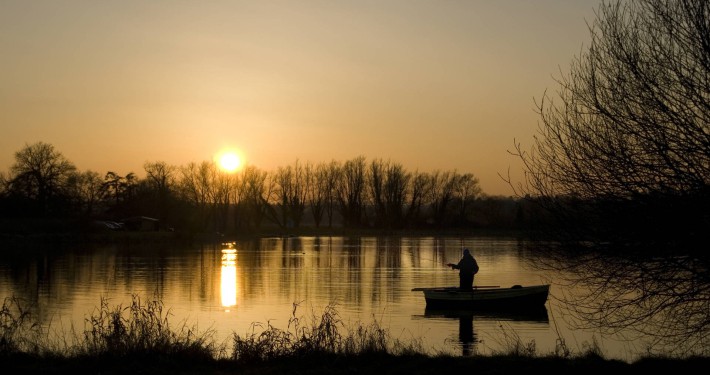 Silhouette of a fishing man on a boat during sunrise